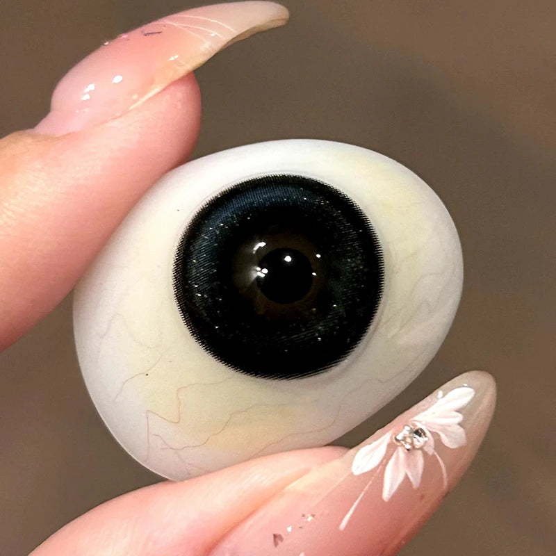Inspecting the rich black tint and delicate shimmer on a fingertip to show the authentic craftsmanship of these lenses.